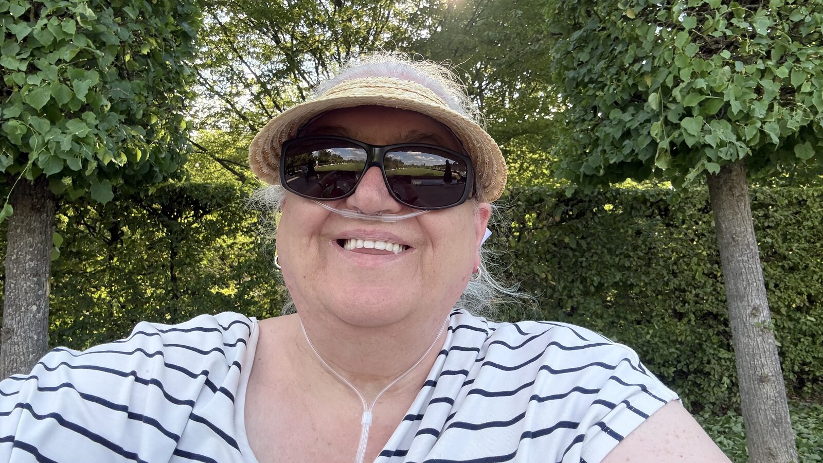 Susanne Steffgen lächelnd mit Strohhut und Sonnenbrille im Park